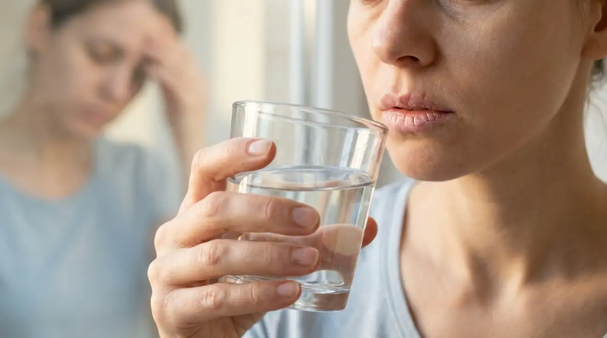 Woman drinking water to relieve dehydration headache and dry lips.